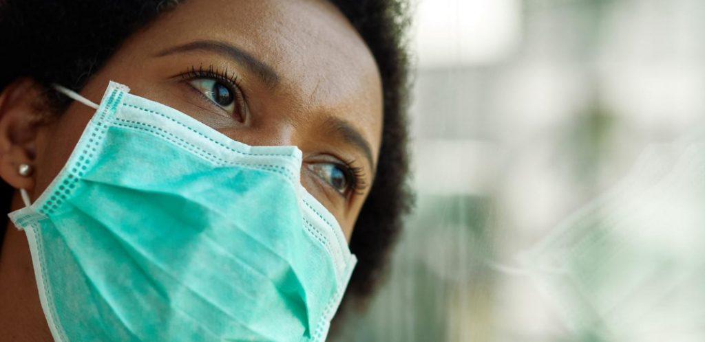 Mulher negra com mascara olha para o horizonte