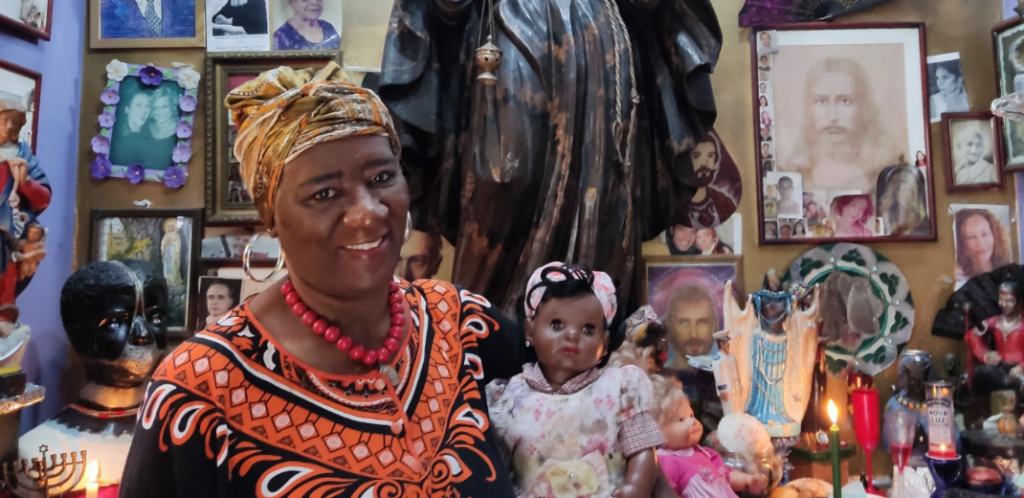 Em uma capela, mulher negra de turbante segura uma boneca negra