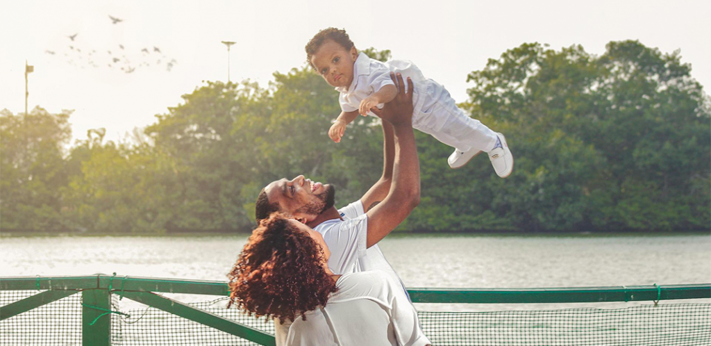 Foto mostra pai jogando criança para cima com a mãe ao lado