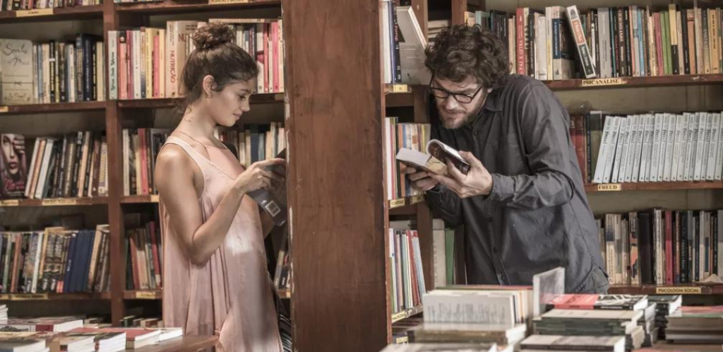 Foto de um casal heterossexual na biblioteca. A cena faz parte da série Todas as mulheres do mundo, da Globo. Emílio, o homem, é claramente um esquerdomacho que confunde amor com tesão