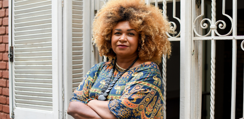 Foto mostra Ediane Maria de braços cruzados em frente a janela