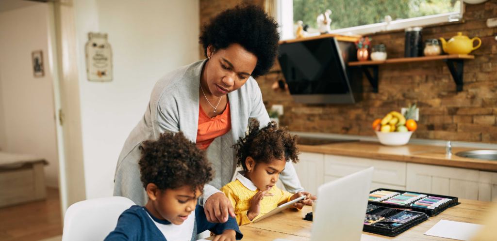 Foto mostra uma mãe realizando uma das tarefas do cuidado: a ajuda aos filhos na educação