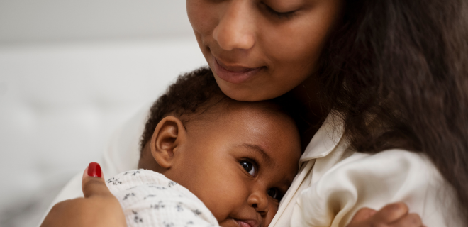 Foto mostra uma das mães cansadas. Com os olhos fechados, ela embala seu bebê