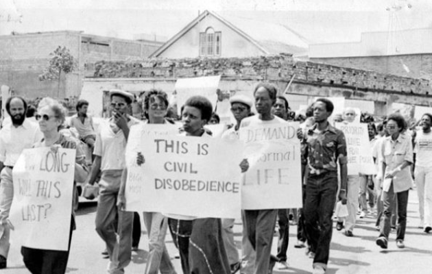 Foto mostra Andaiye, ativista feminista guianense, segurando cartaz com os dizeres 