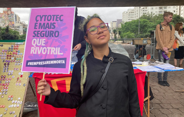 Foto mostra mulher segurando uma placa com o texto 