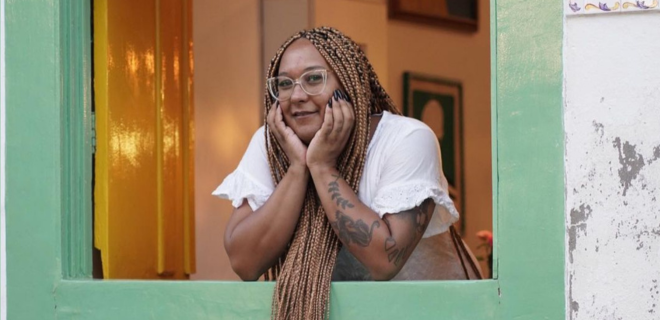 Foto mostra Isa sorrindo apoiada em janela