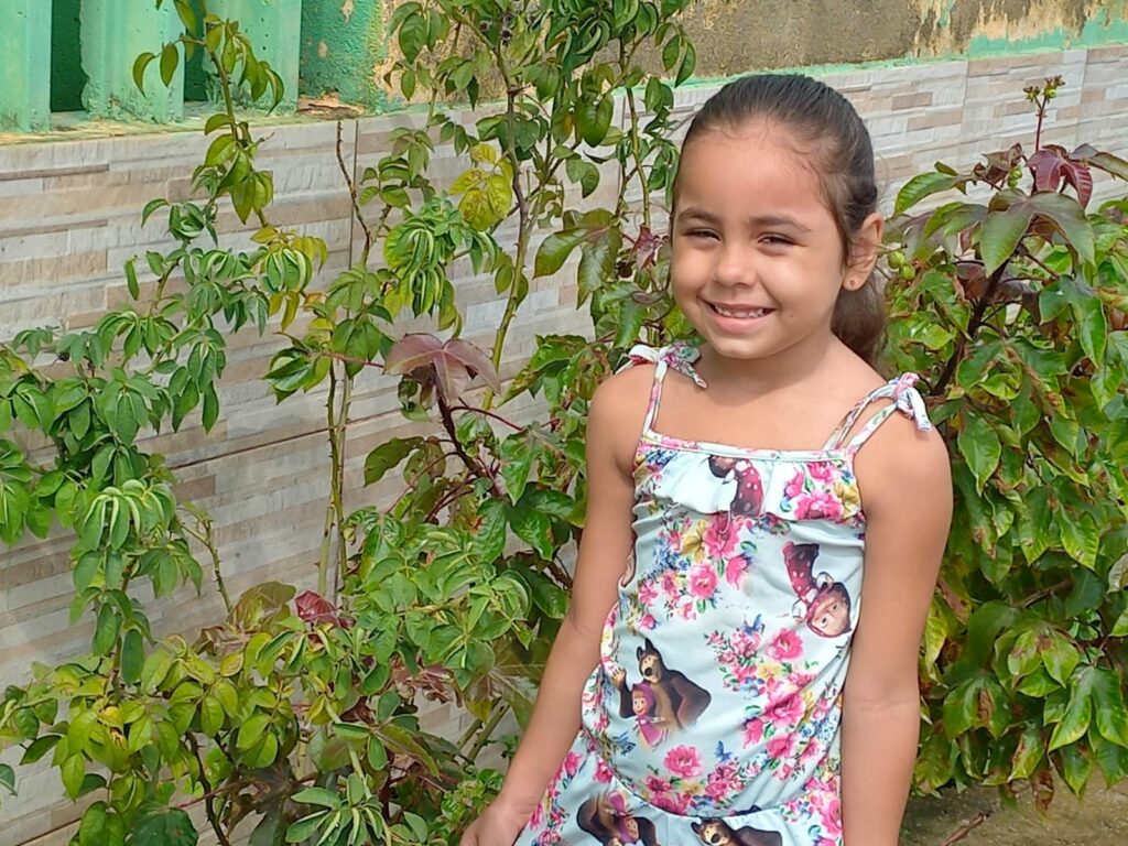 Foto mostra Ester sorrindo perto de plantas