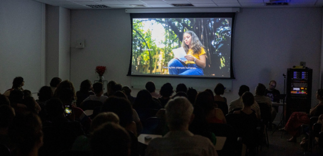 Foto mostra telão exibindo o primeiro episódio da série O mundo que sei
