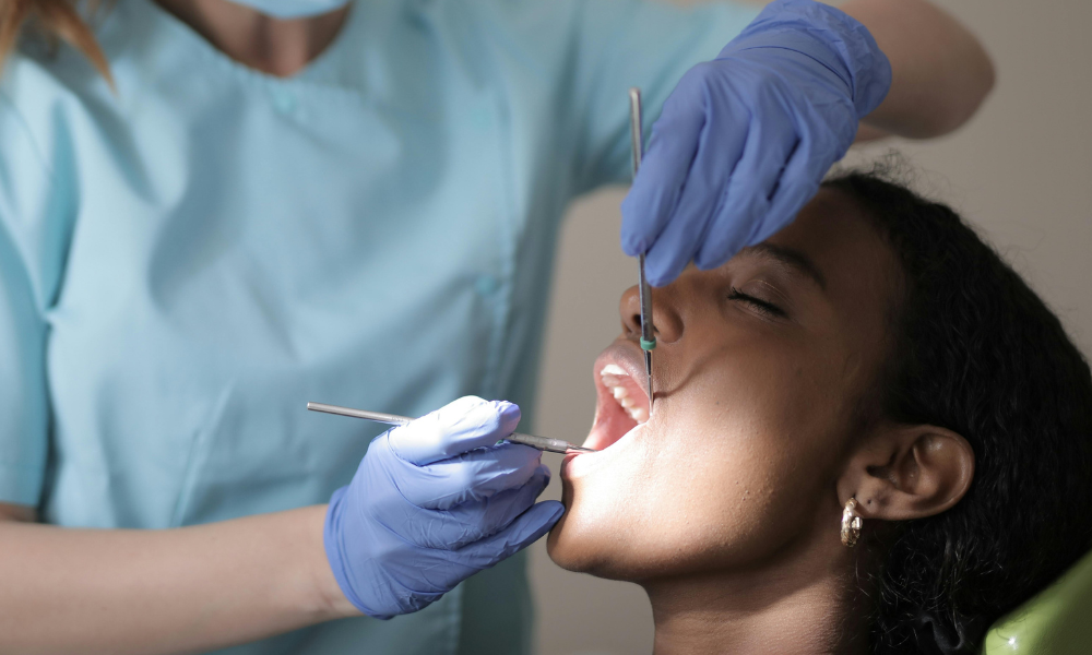 Foto mostra mulher negra sendo atendida por dentista, simbolizando paciente de reconstrução dentária pelo SUS