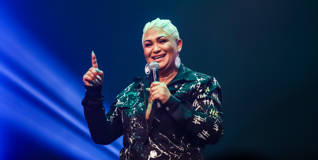 muler negra sorrindo segurando microfone e apontando o dedo para cima