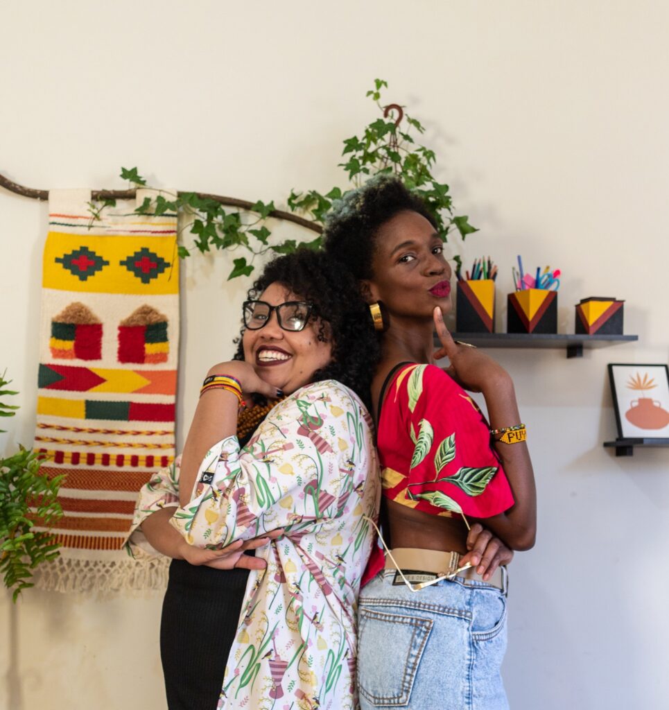 duas mulheres negras posam para foto de costas uma para outra