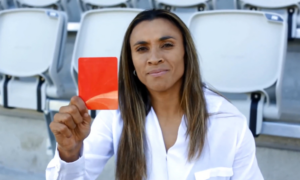 Foto mostra a jogadora Marta dando cartão vermelho para a violência doméstica