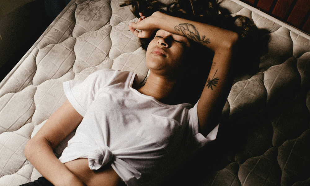 Foto mostra mulher durante a menstruação, deitada com a mão na cabeça e na barriga