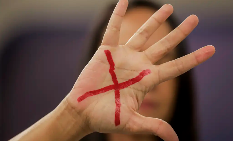 mulher mostra palma da mão com um X em vermelho; violência doméstica