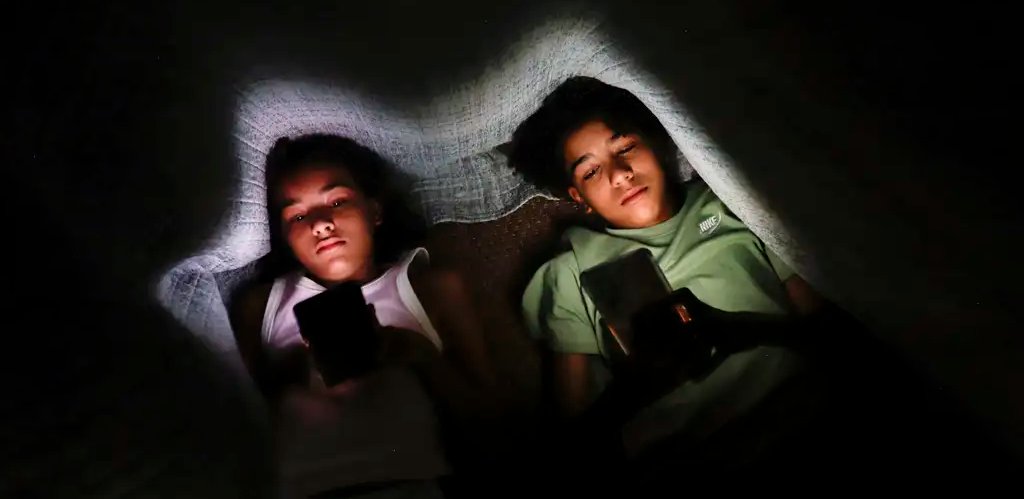 duas crianças usando o celular em baixo do cobertor