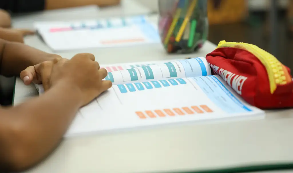 braços de criança em cima de livro escolar