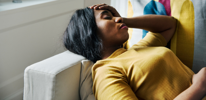 Foto mostra mulher com endometriose com a mão na barriga e na cabeça
