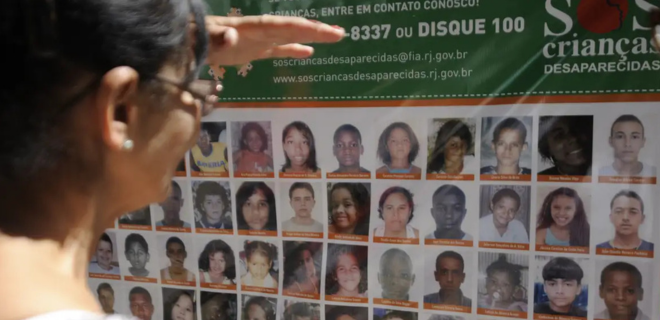 Foto mostra mulher olhando para cartaz com fotos de crianças desaparecidas